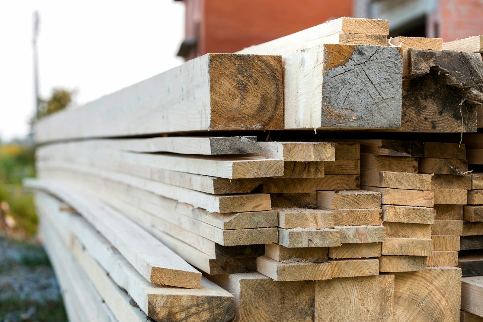 Close-up of piled stack of natural brown uneven rough wooden boards lit by bright sun. Industrial